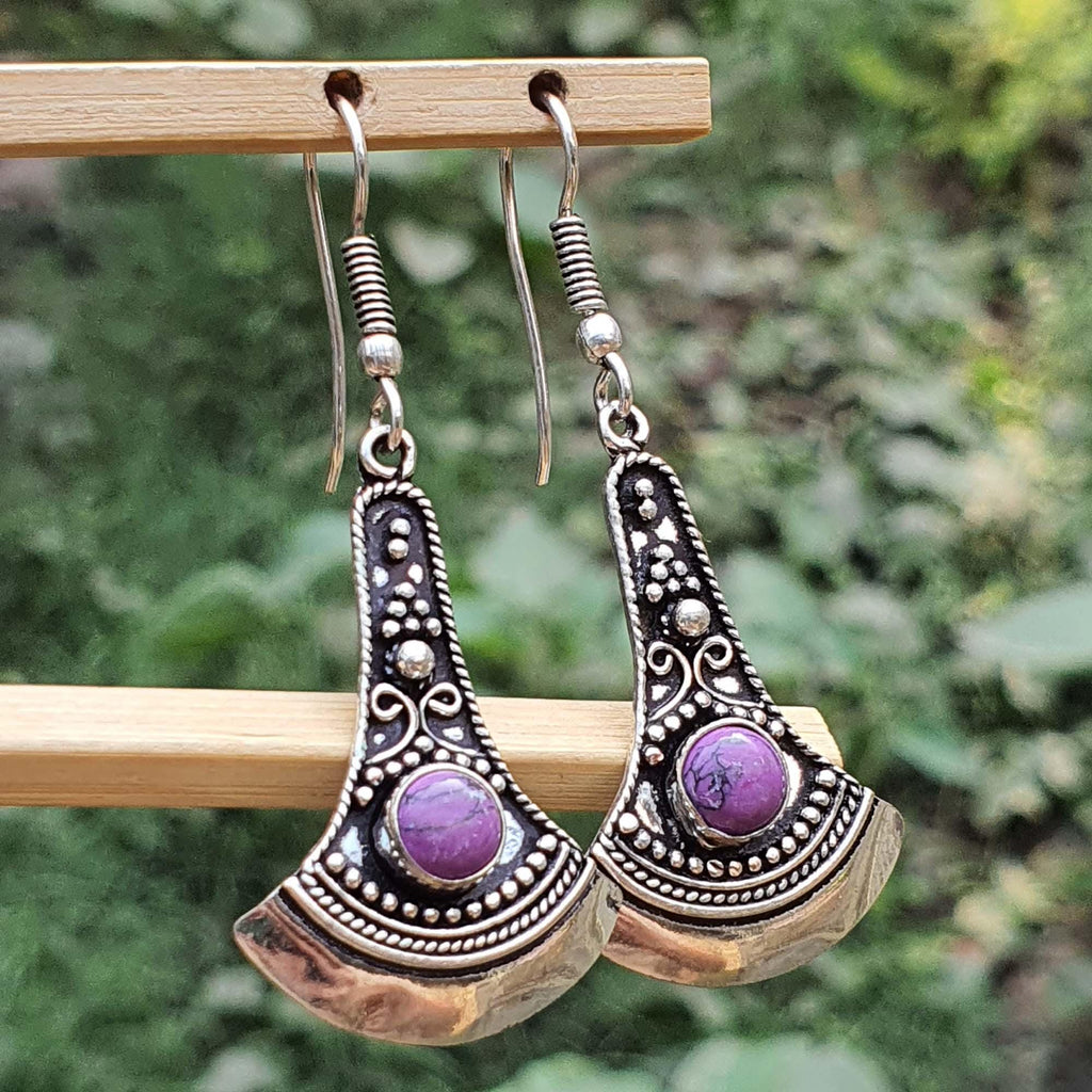 Silver earrings with purple stones on a wooden stand against a blurred green background