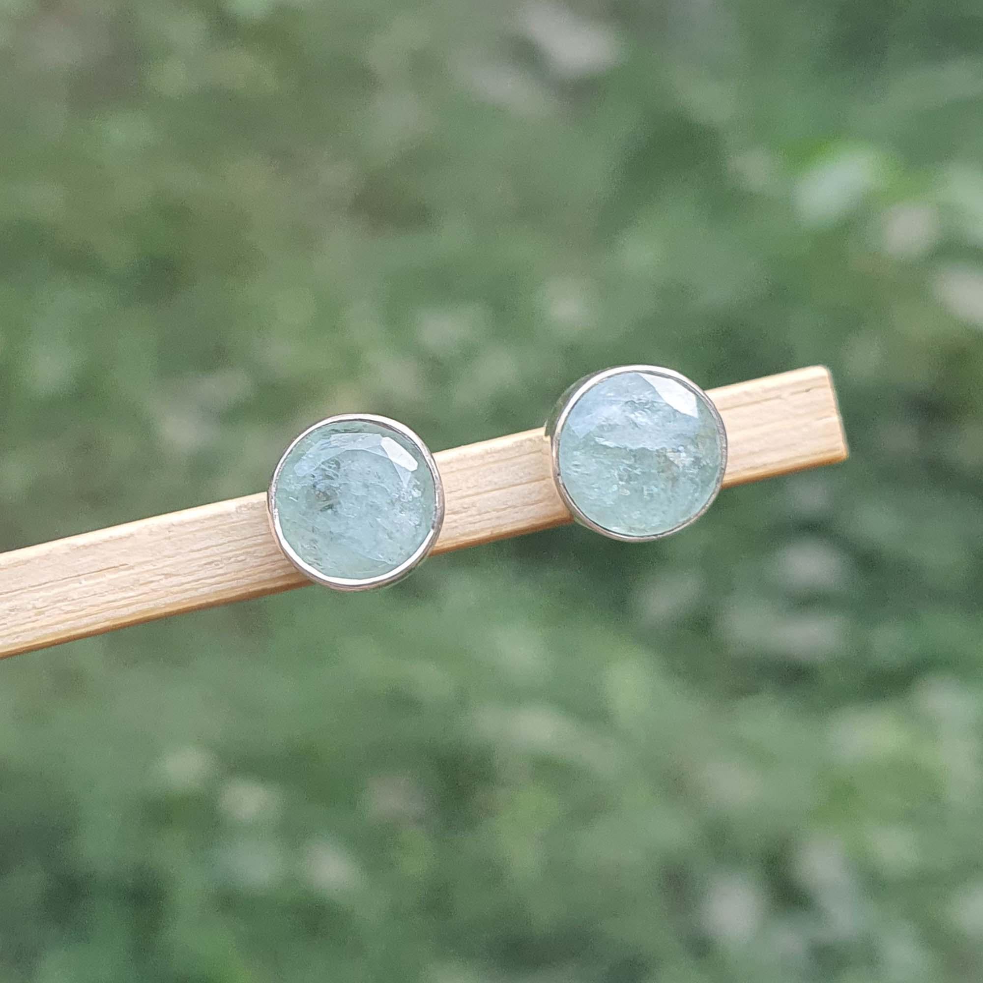 Pair of round earrings with a light blue gemstone on a wooden stick against a blurred green background