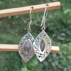 Silver filigree earrings with gemstones hanging on a wooden stick against a blurred green background