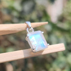 Silver pendant with a rainbow moonstone on a wooden stick against a blurred natural background