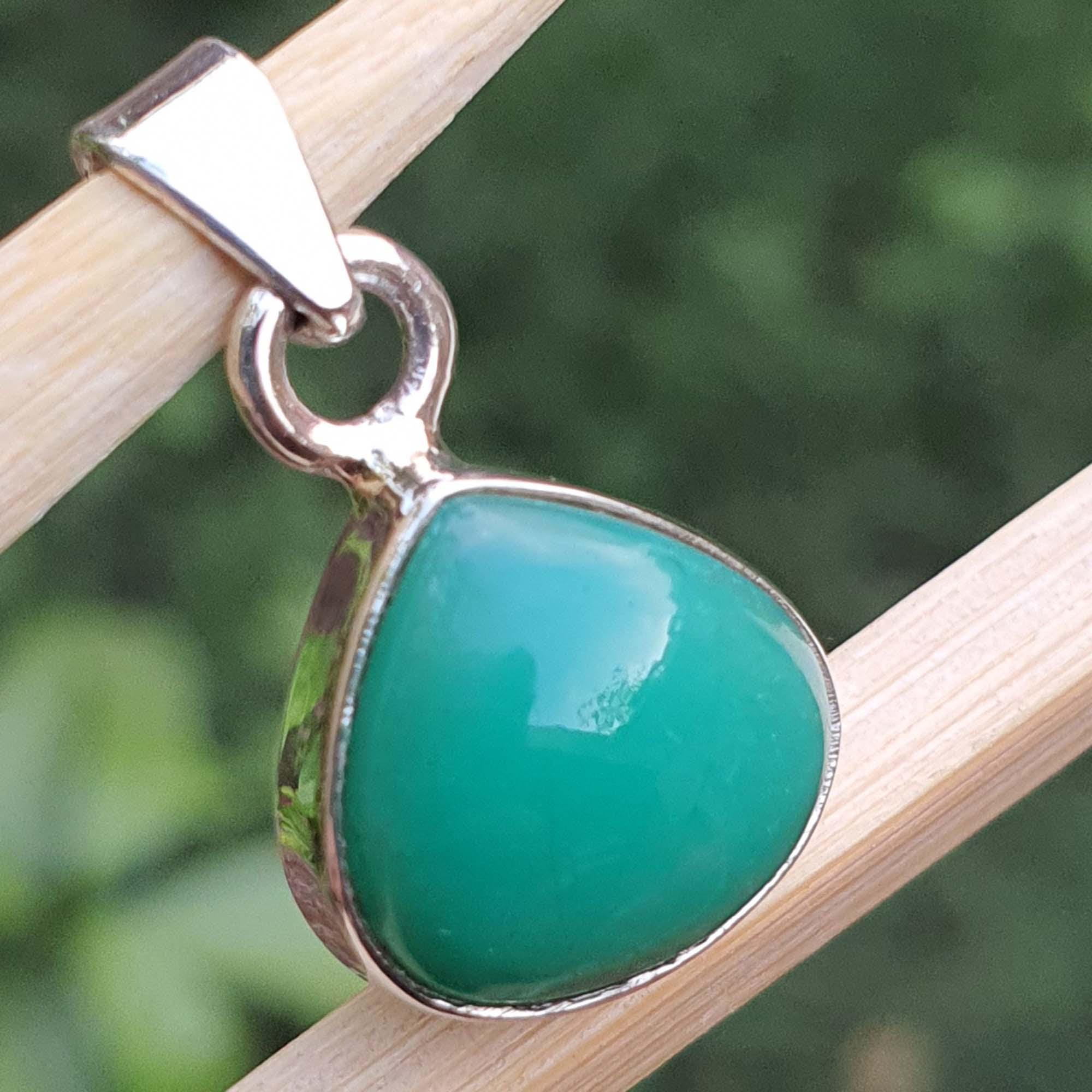 Teal pendant with silver setting on a wooden stick against a blurred green background