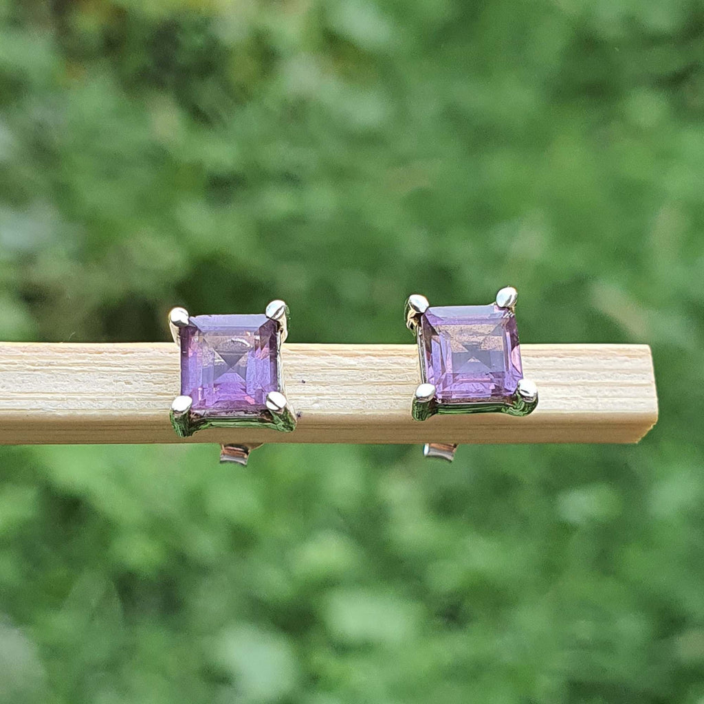 Pair of square purple gemstone earrings on a wooden stick with a green blurred background