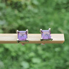 Pair of square purple gemstone earrings on a wooden stick with a green blurred background
