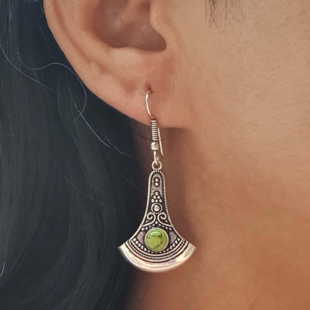 Silver earring with green gemstone worn by a person