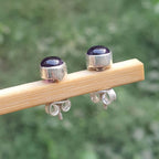 Silver earrings with purple stones on a wooden stick against a blurred green background