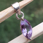 Silver pendant with a purple gemstone on a wooden stick against a blurred green background