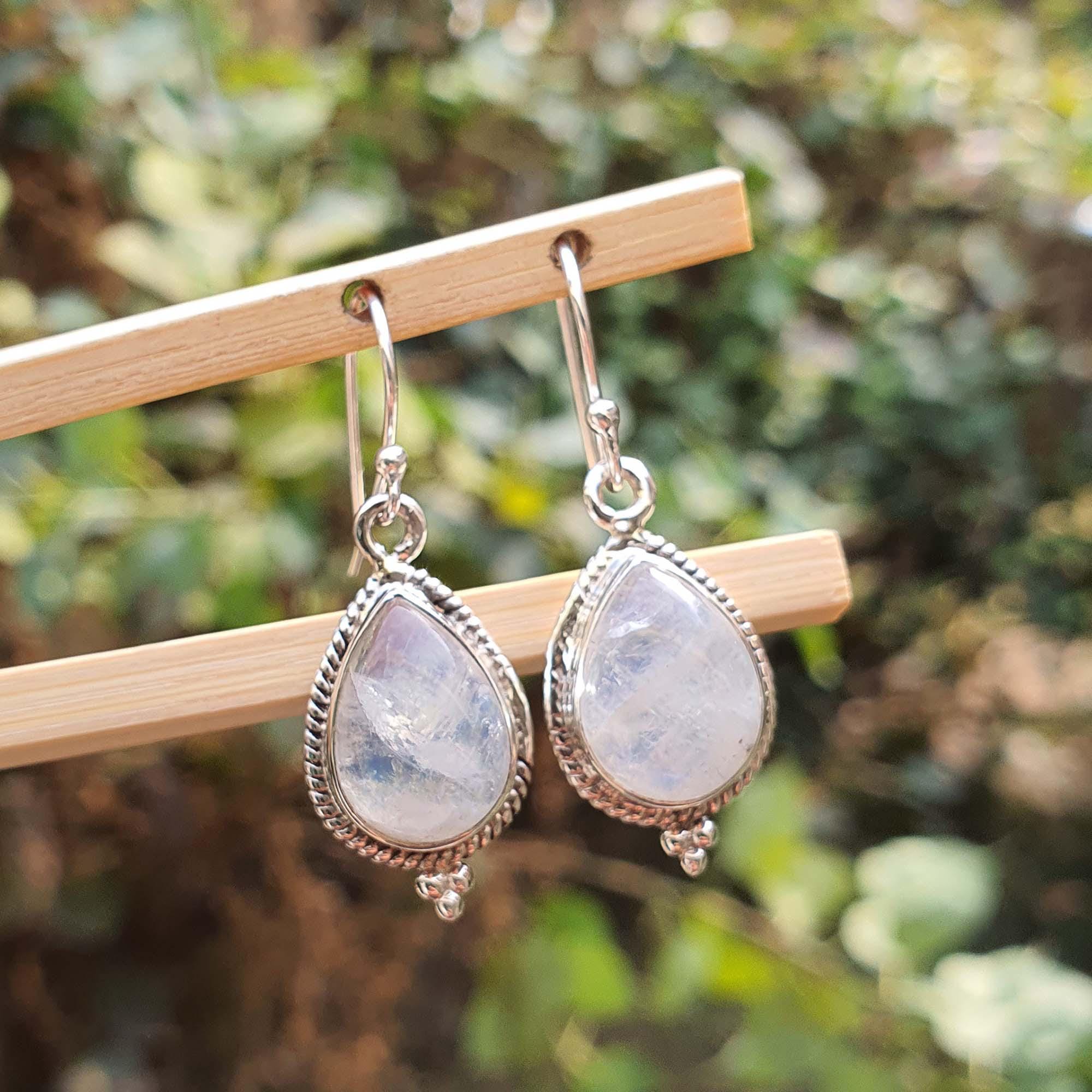 Teardrop-shaped earrings with silver frames on a wooden stand against a blurred green background