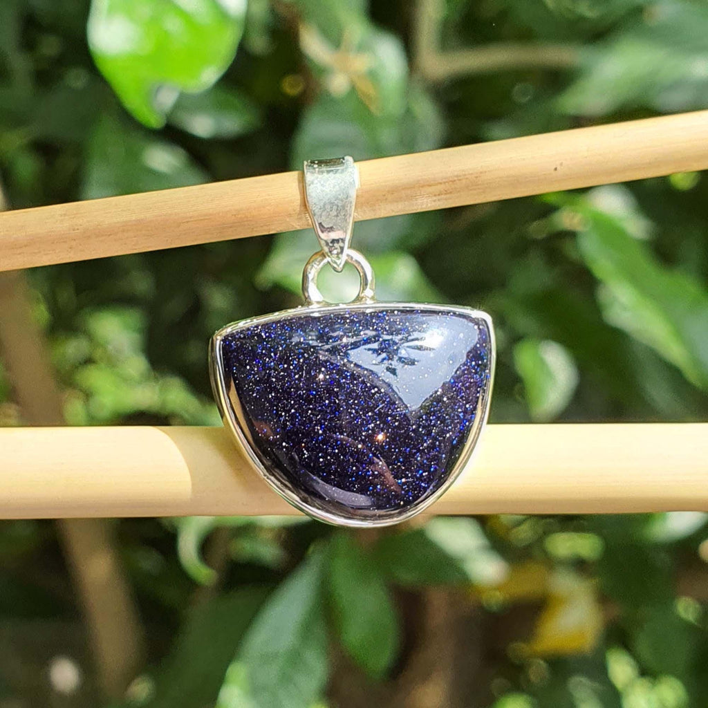Blue stone pendant on a silver chain against a green leafy background