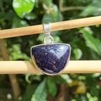 Blue stone pendant on a silver chain against a green leafy background