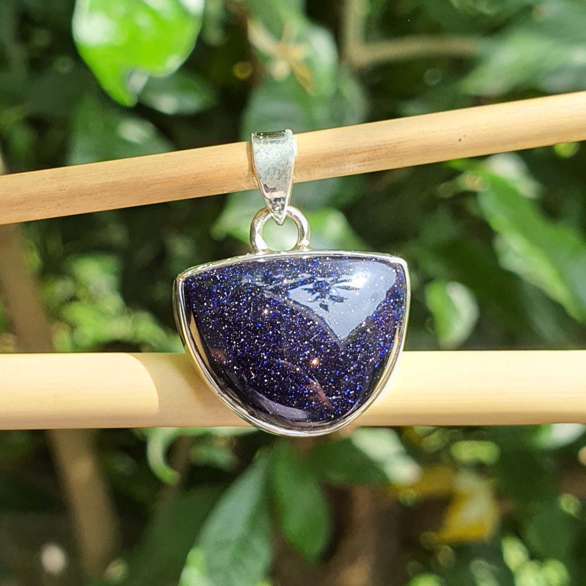 Blue stone pendant on a silver chain against a green leafy background