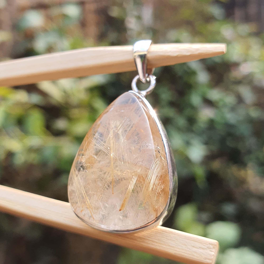 Teardrop-shaped pendant with a textured stone on a wooden stick against a blurred green background
