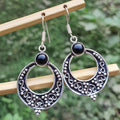 Silver earrings with black stones on a wooden stick against a blurred green background