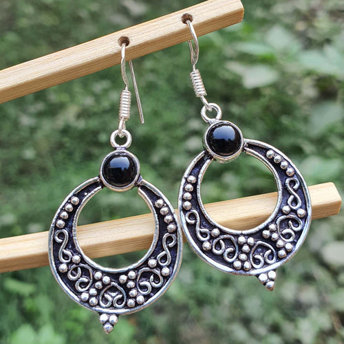 Silver earrings with black stones on a wooden stick against a blurred green background