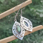 Silver earrings with gemstones on a wooden stick against a blurred green background