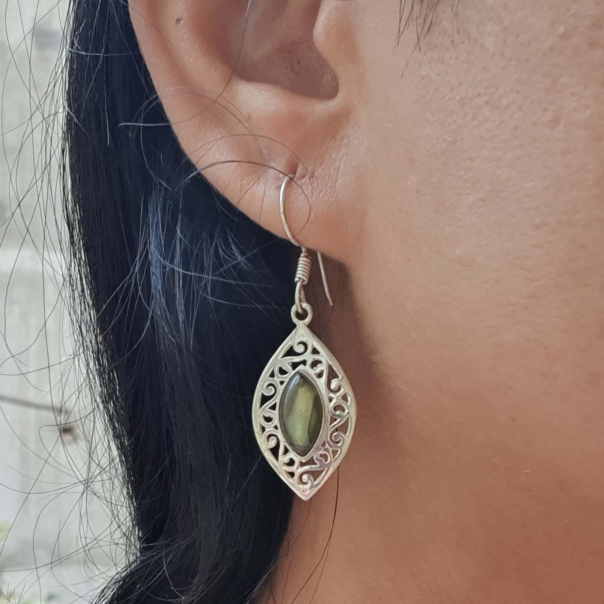 Close-up of an ear wearing a silver earring with a green gemstone.