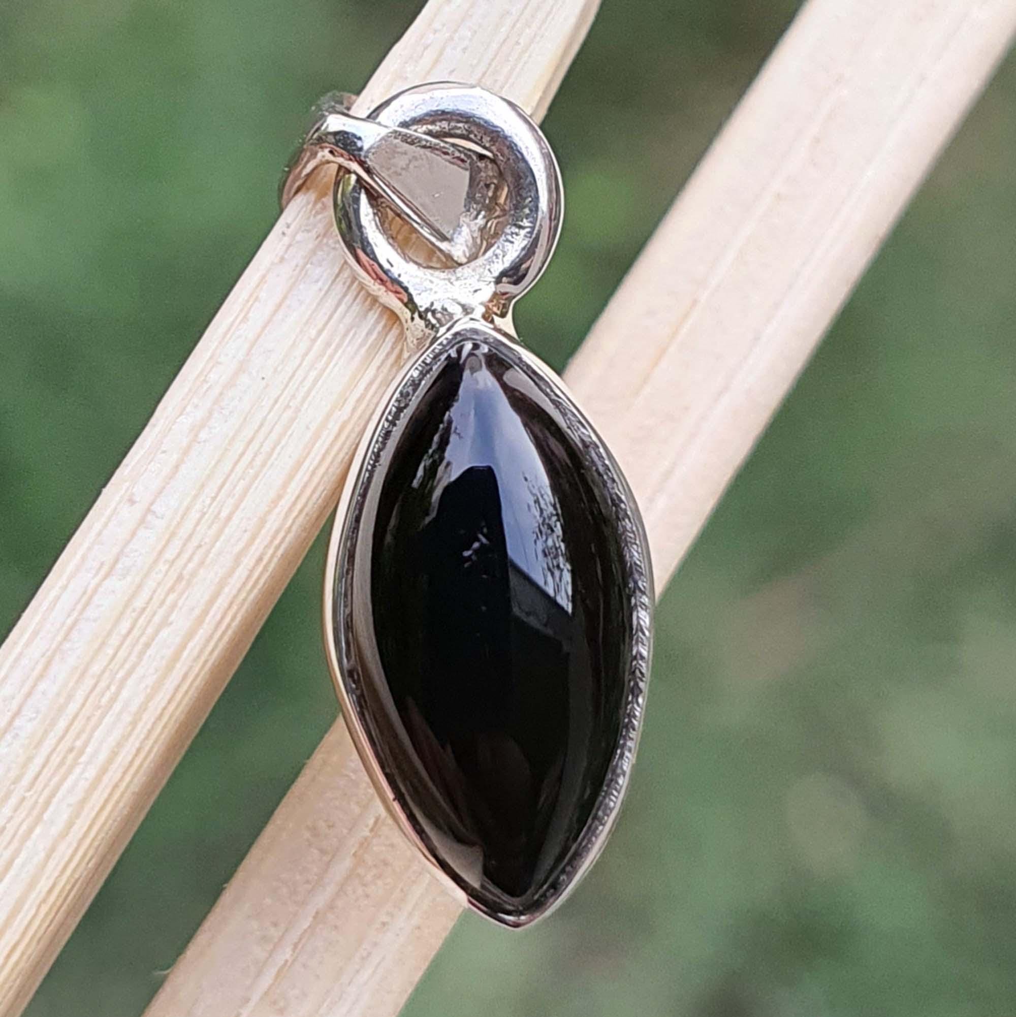 Black teardrop pendant on a silver setting against a blurred natural background