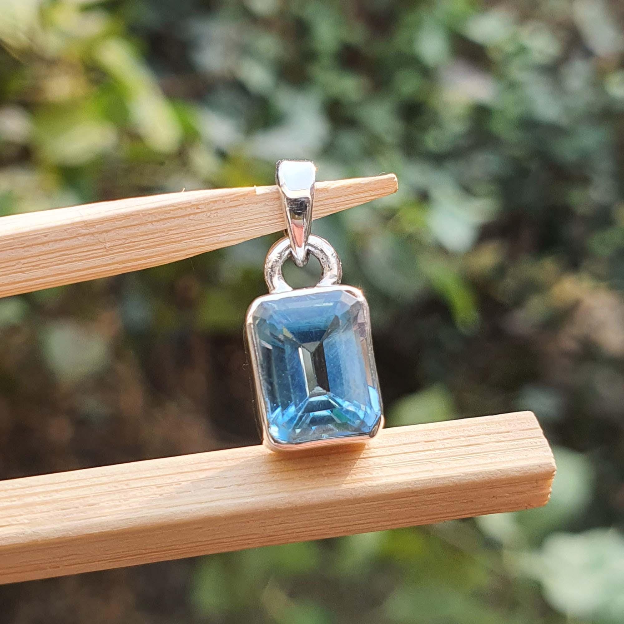 Silver pendant with a blue gemstone on a wooden stand against a blurred green background
