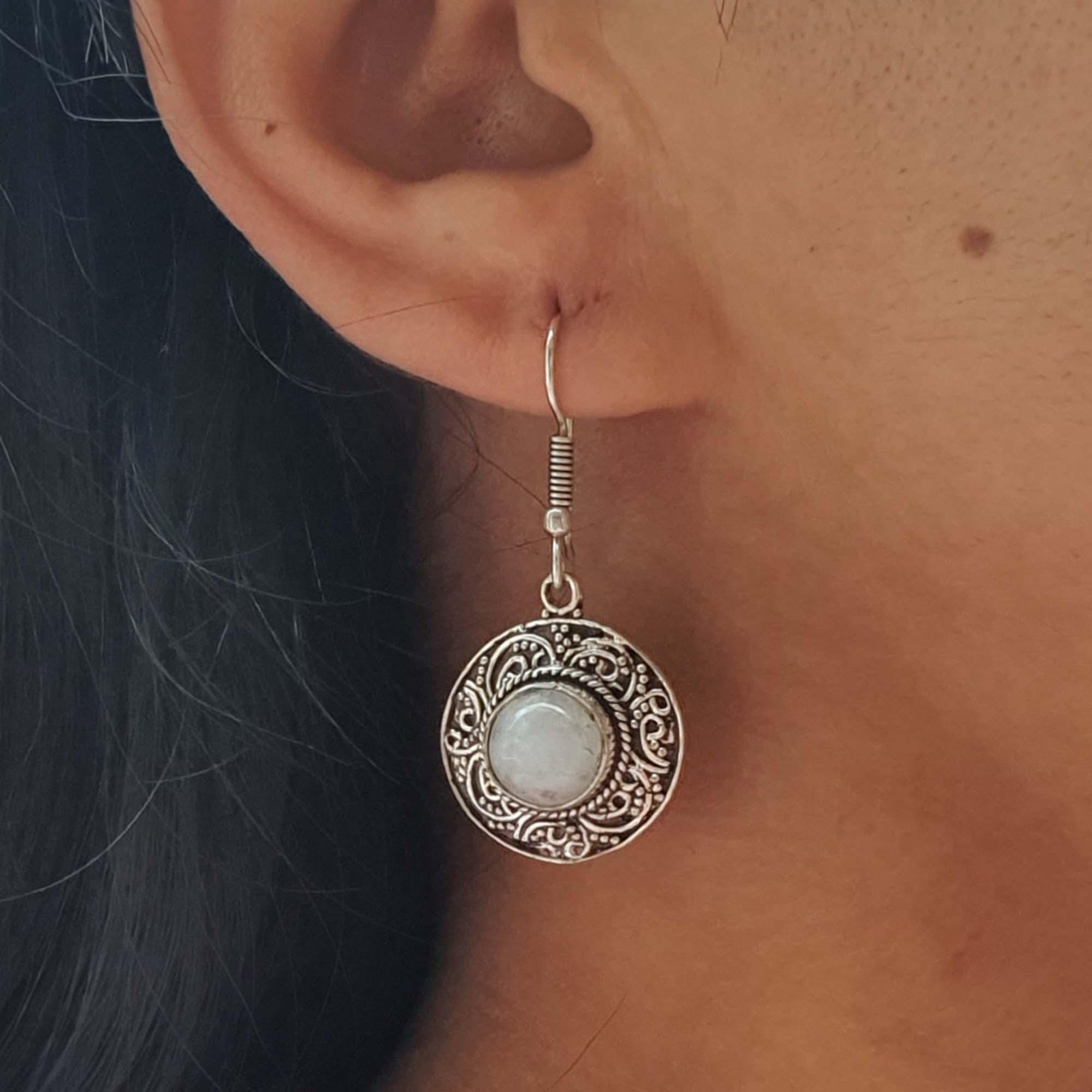 Close-up of an ear wearing a decorative silver earring with a light stone center.