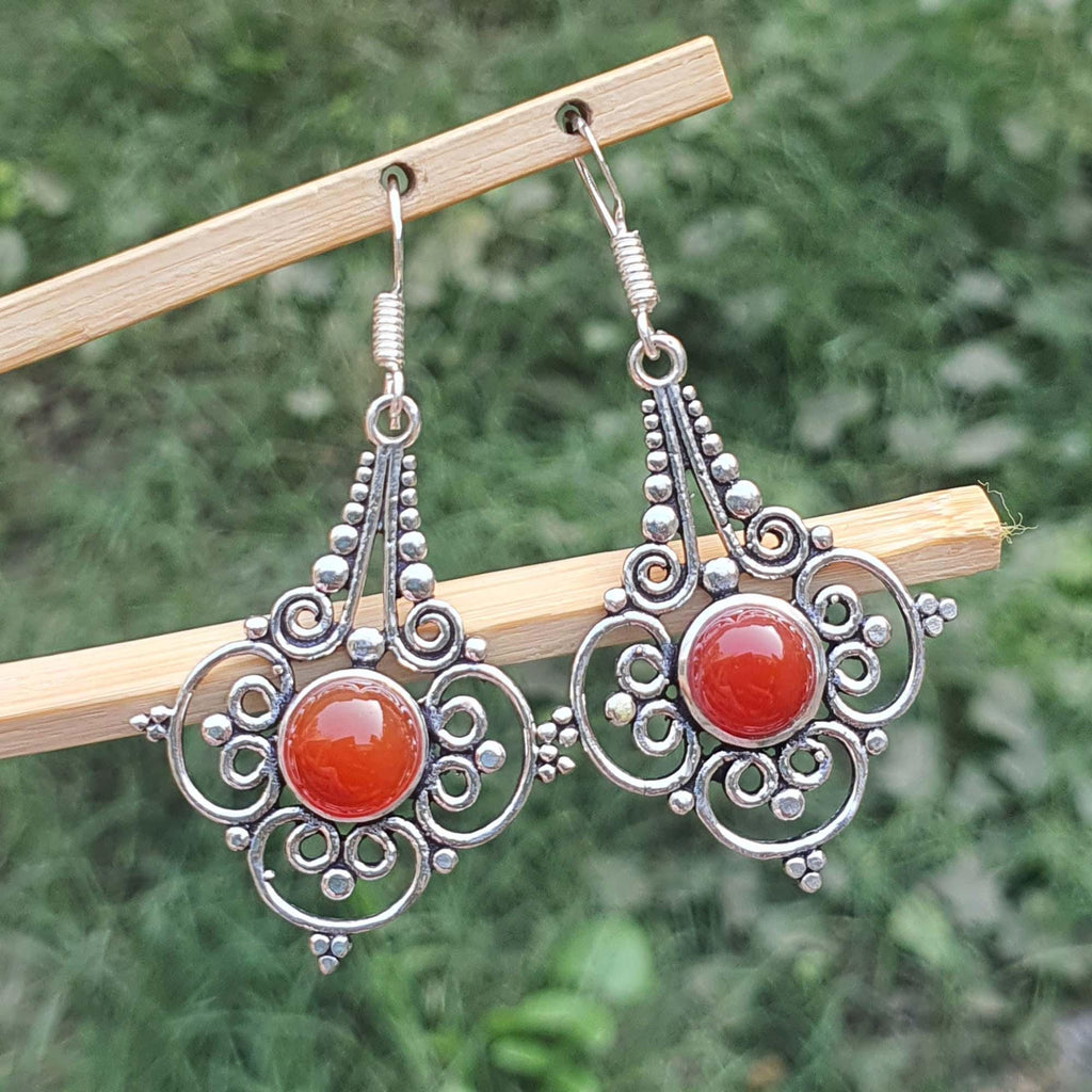 Silver earrings with red stones on a wooden stick against a green background