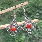 Silver earrings with red stones on a wooden stick against a green background