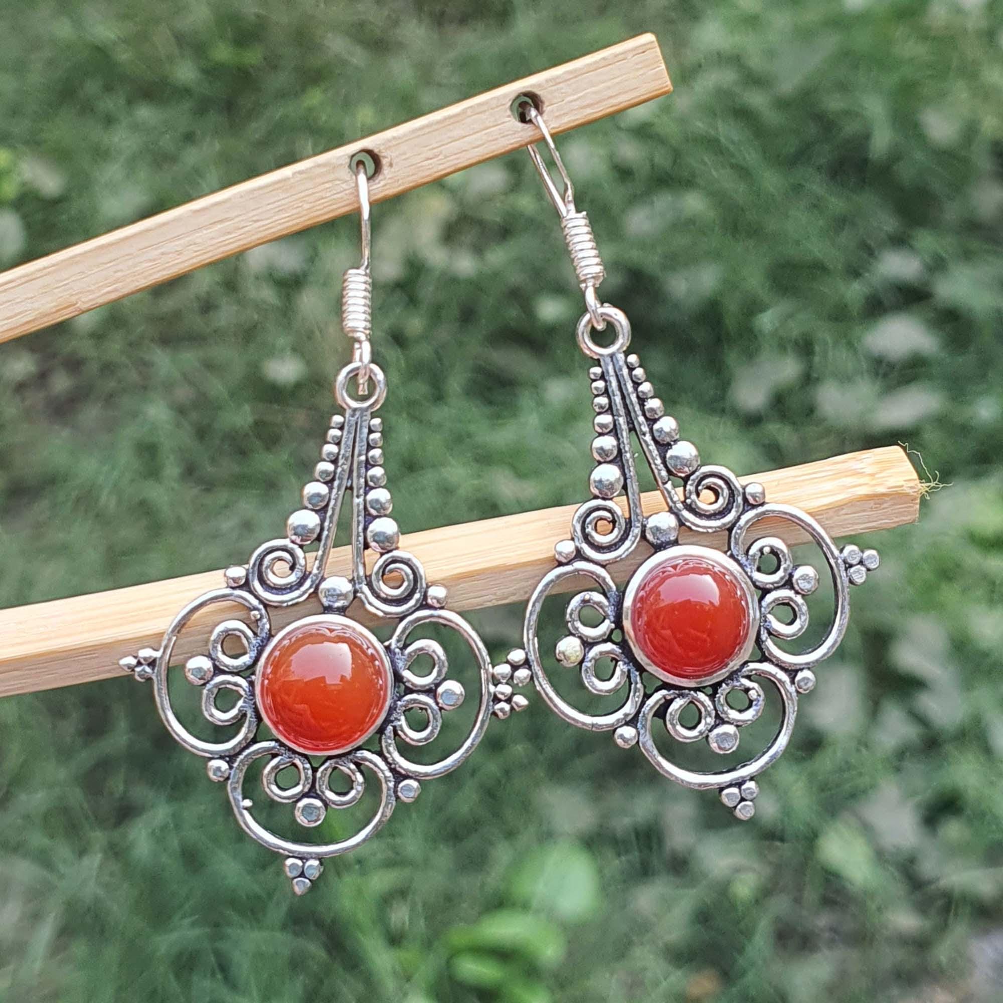 Silver earrings with red stones on a wooden stick against a green background