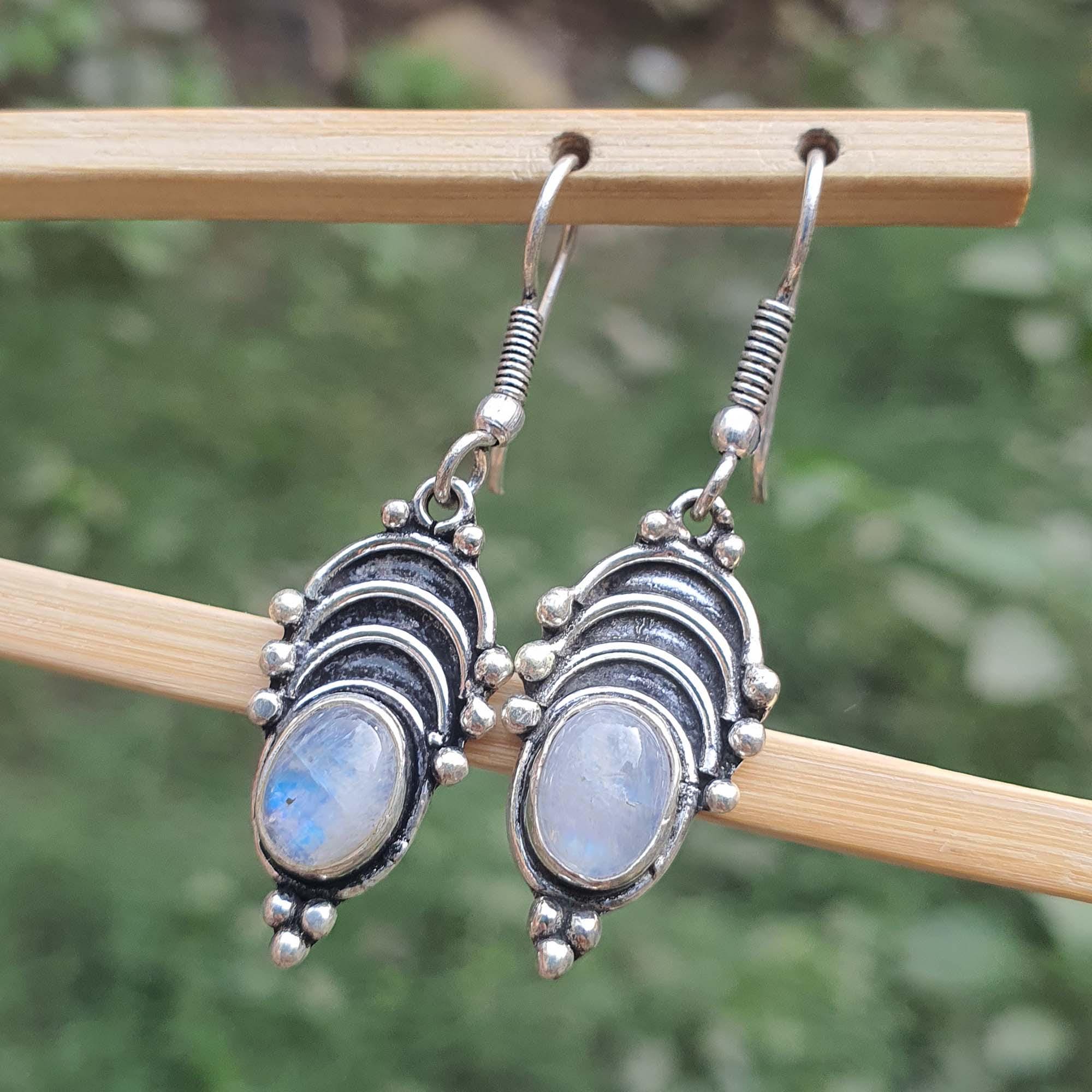 Silver earrings with gemstones on a wooden stick against a blurred green background