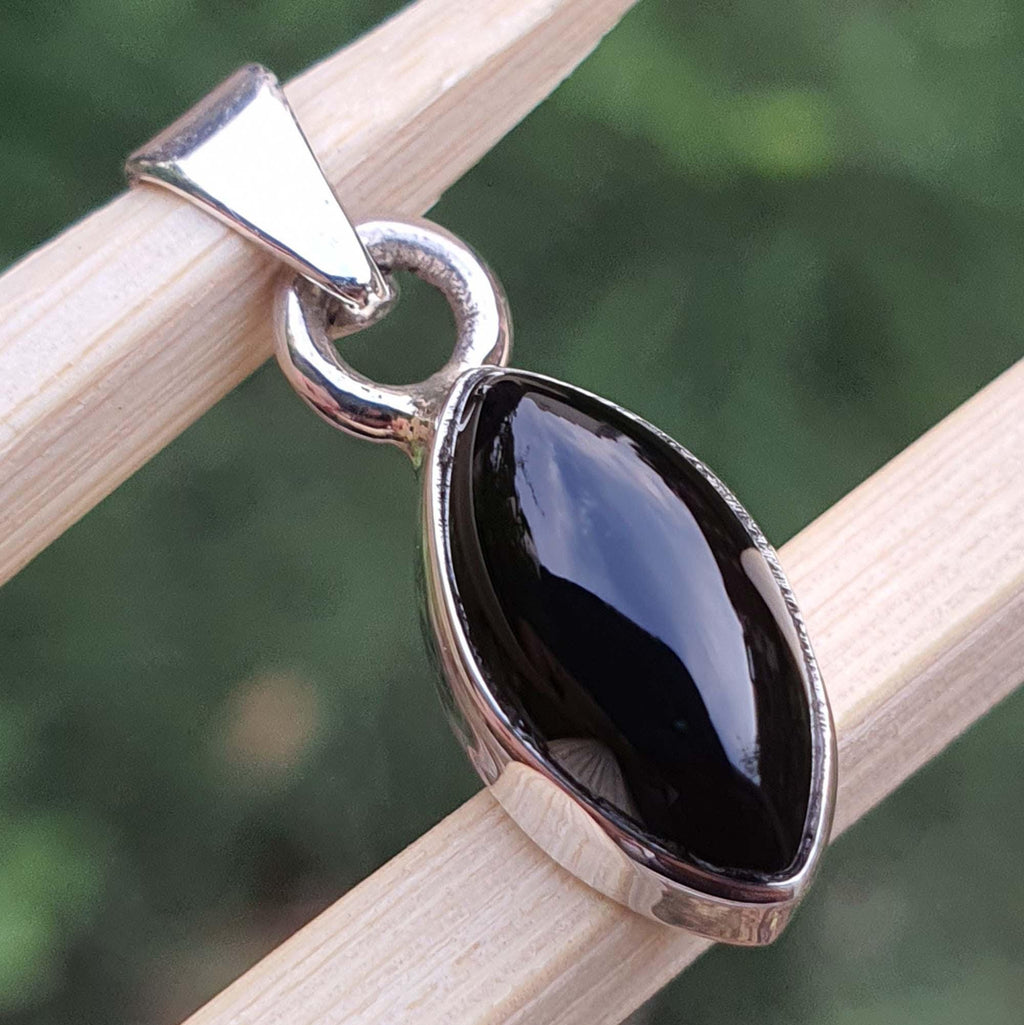 Black teardrop pendant on a silver chain against a blurred green background