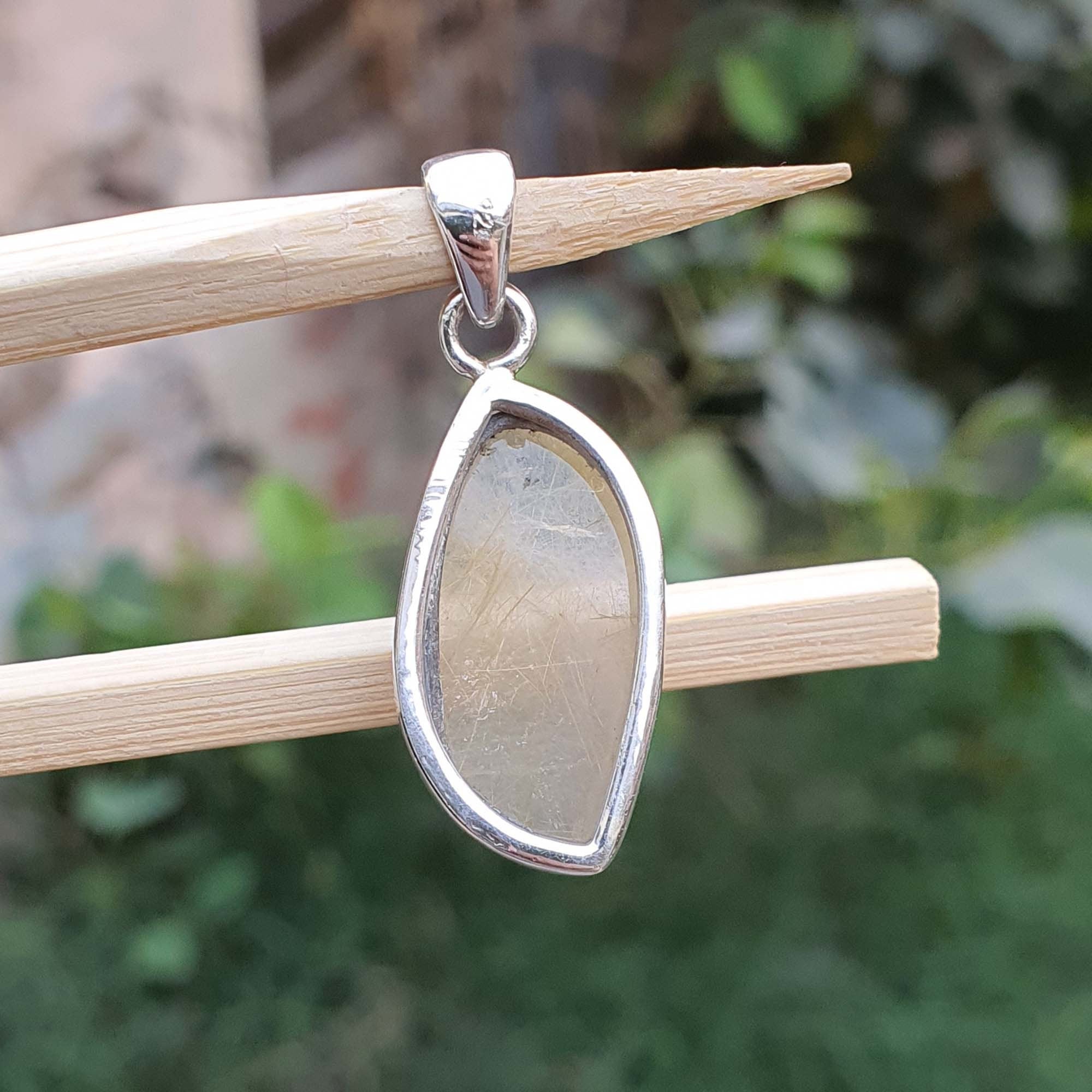 Teardrop-shaped silver pendant on a stick with a blurred green background