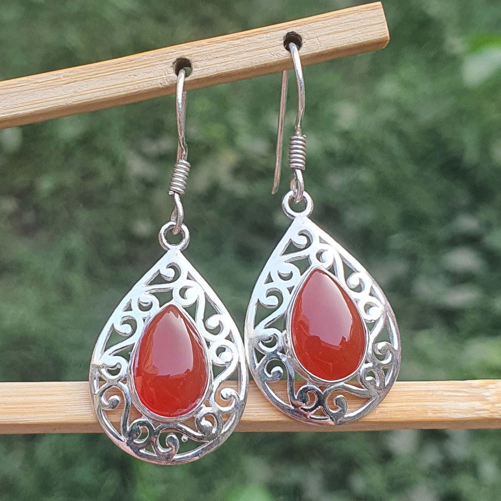 Silver earrings with red teardrop stones on a wooden stick against a blurred green background