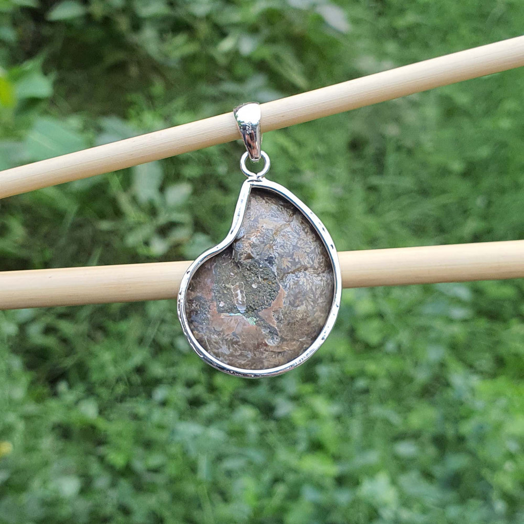 Teardrop-shaped pendant with natural stone design on a stick against a green background