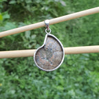 Teardrop-shaped pendant with natural stone design on a stick against a green background