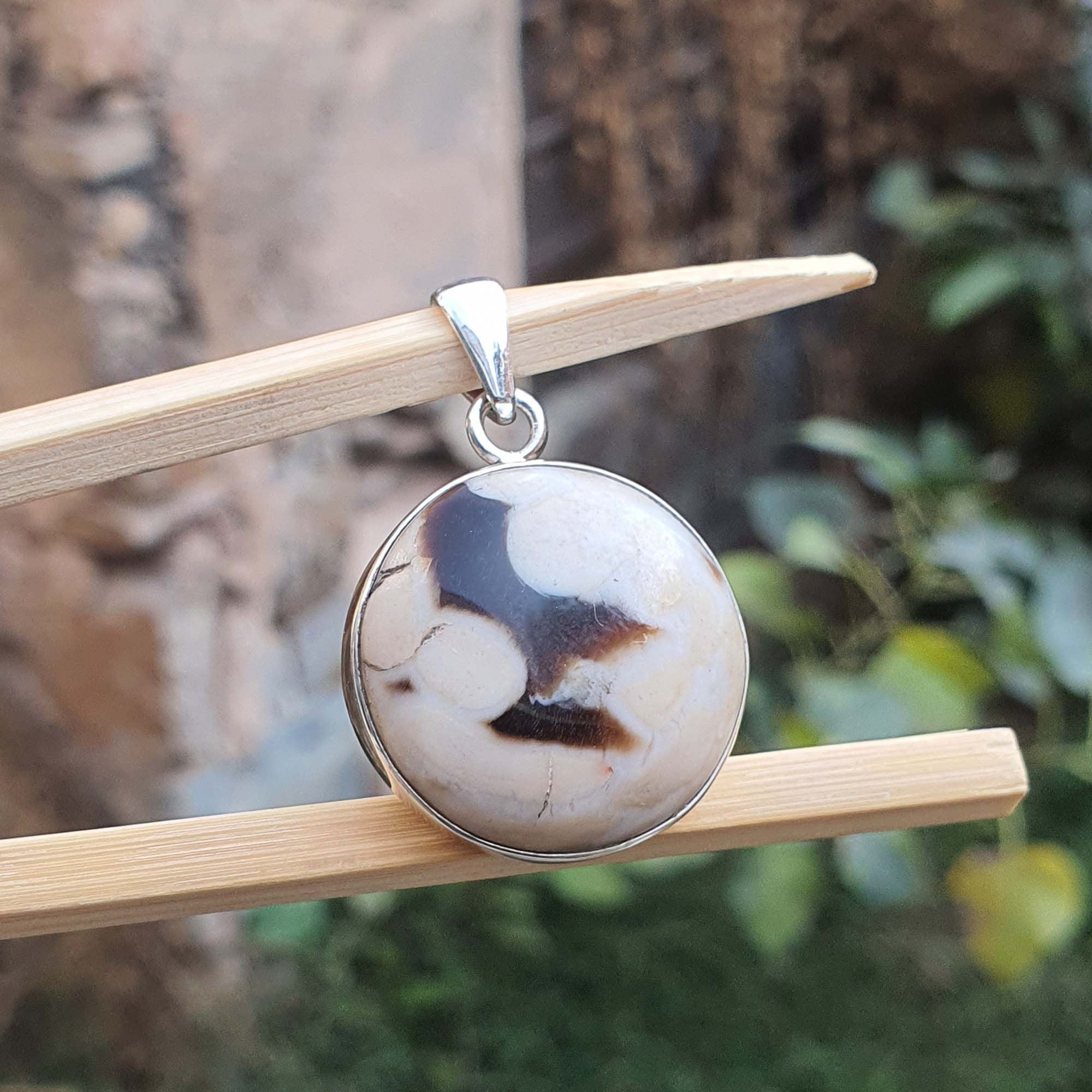 Round pendant with marbled design on a wooden stick against a natural background