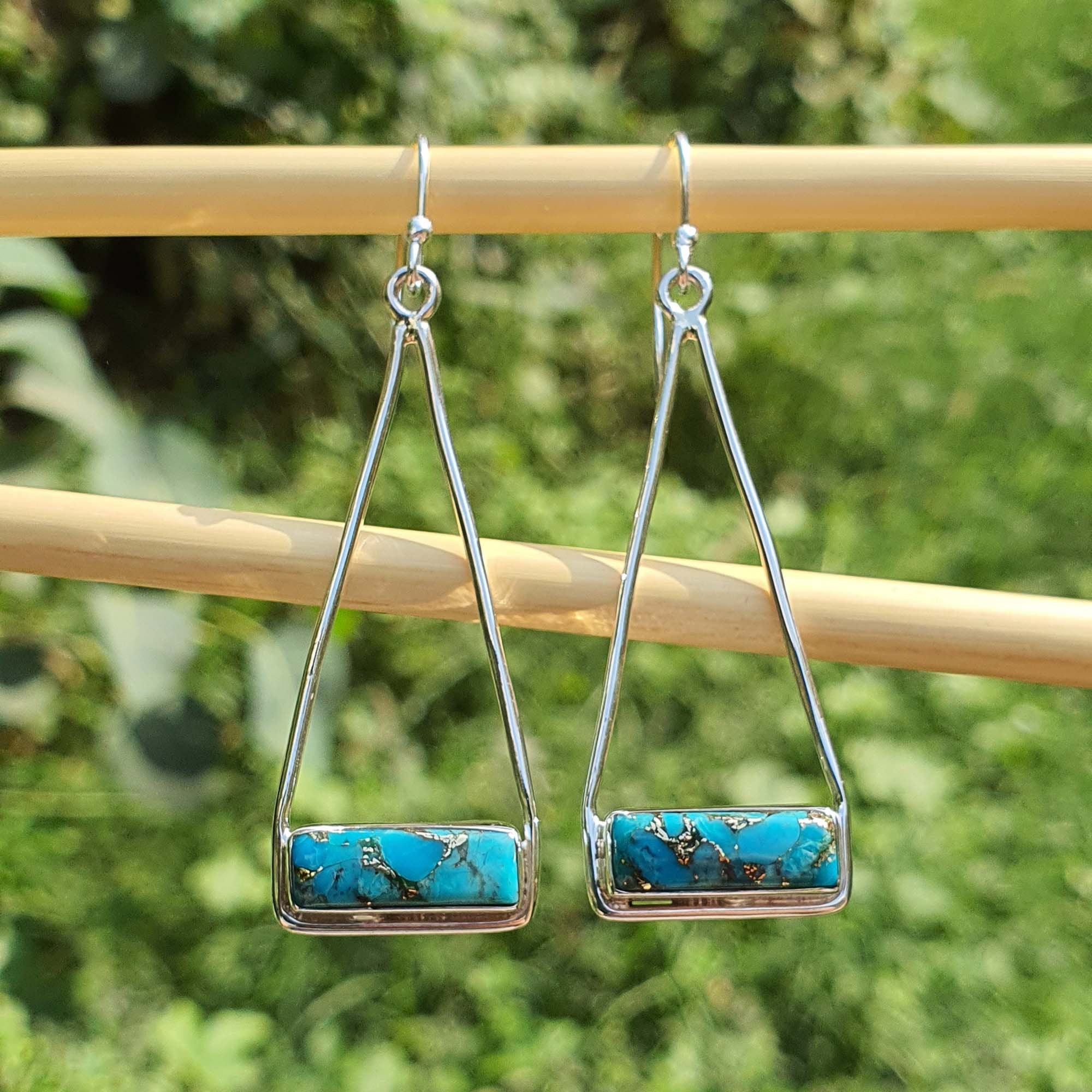 Turquoise bar earrings on a wooden stick with a green foliage background