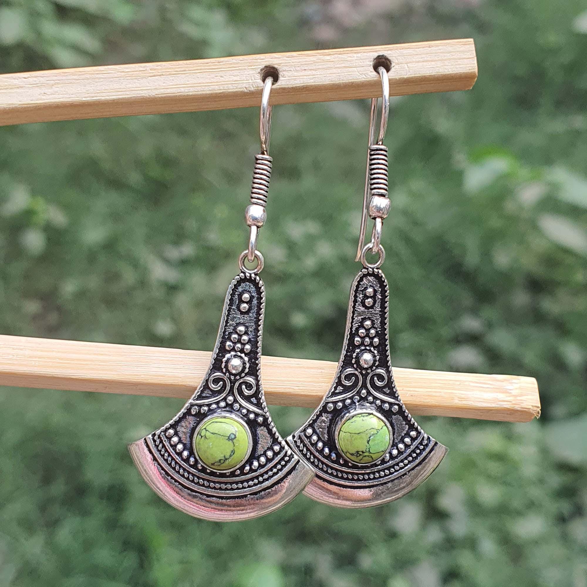 Pair of silver earrings with green stones on a wooden stick against a blurred green background