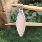 Pink stone pendant with silver frame on a wooden stick against a natural background