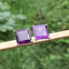 Pair of purple square gemstone earrings on a stick with a green blurred background