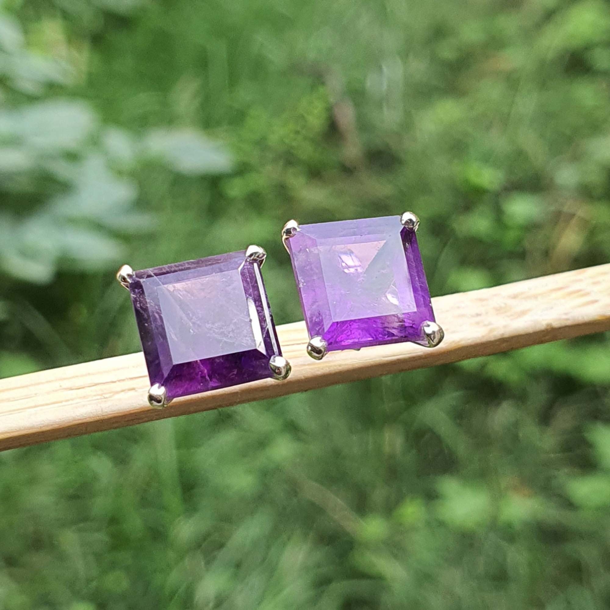 Pair of purple square gemstone earrings on a stick with a green blurred background
