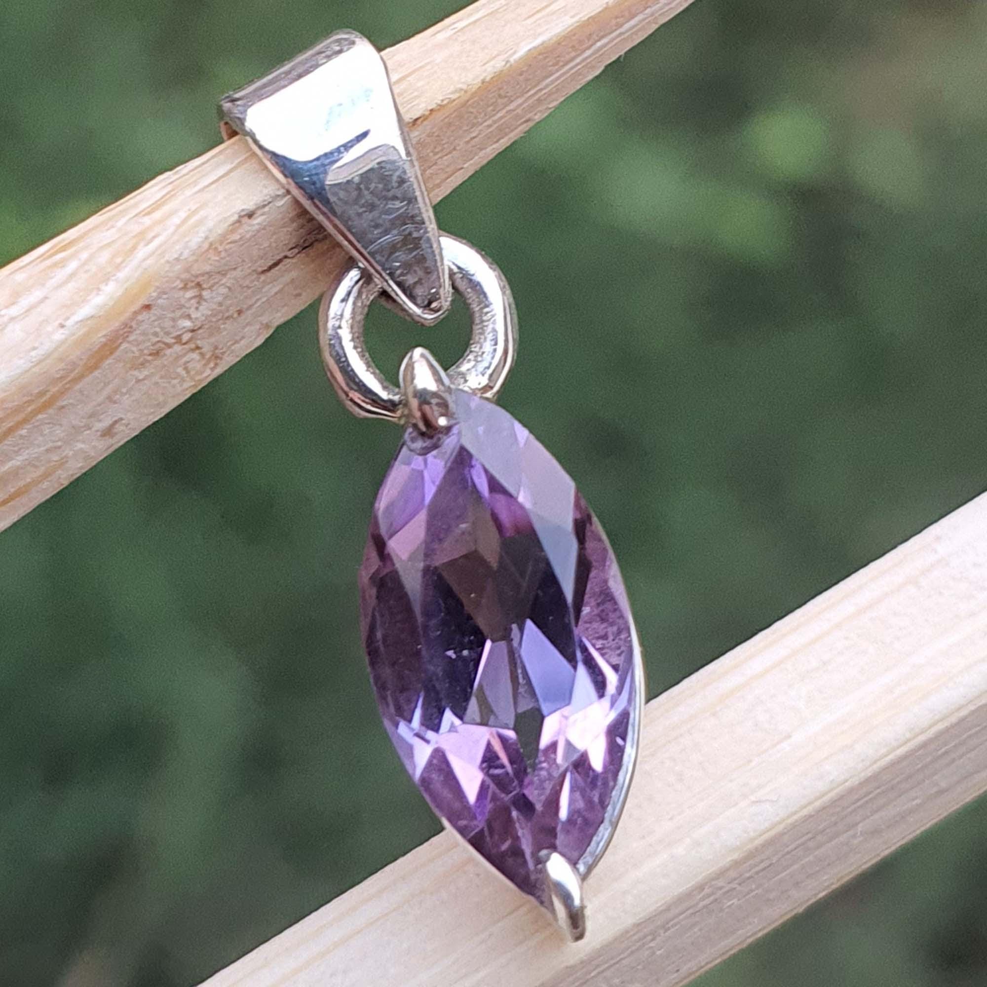 Purple teardrop pendant on a silver chain against a blurred green background