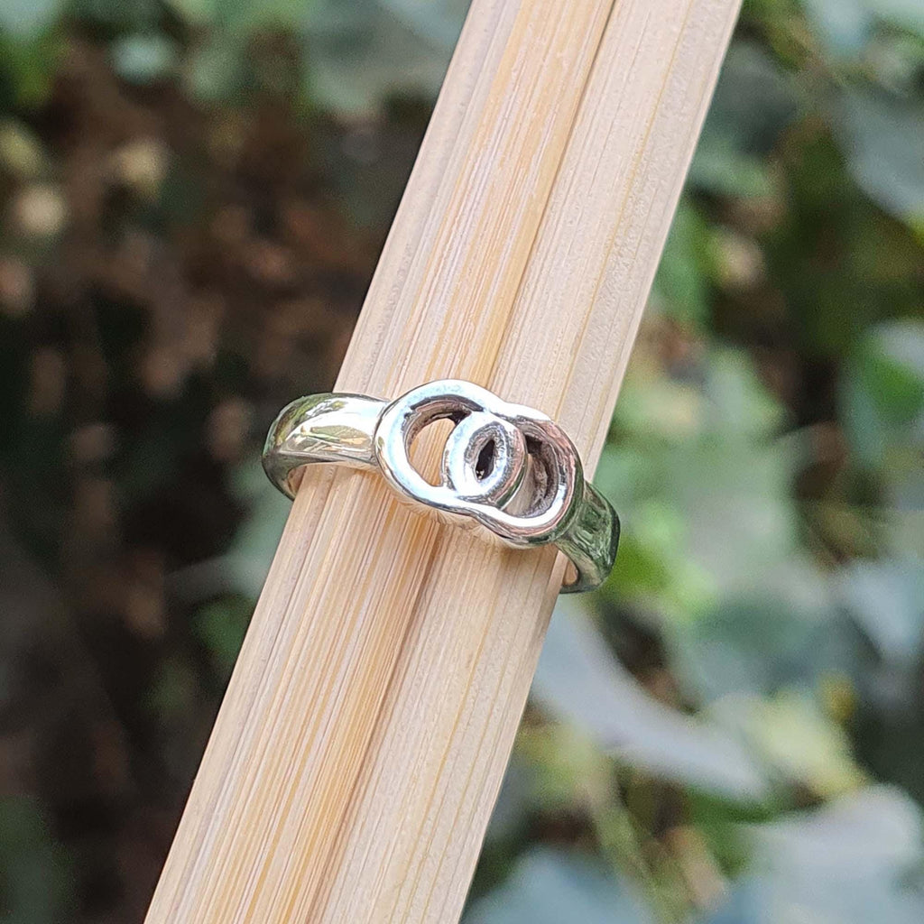 Silver ring with a unique design on a wooden stick against a blurred natural background