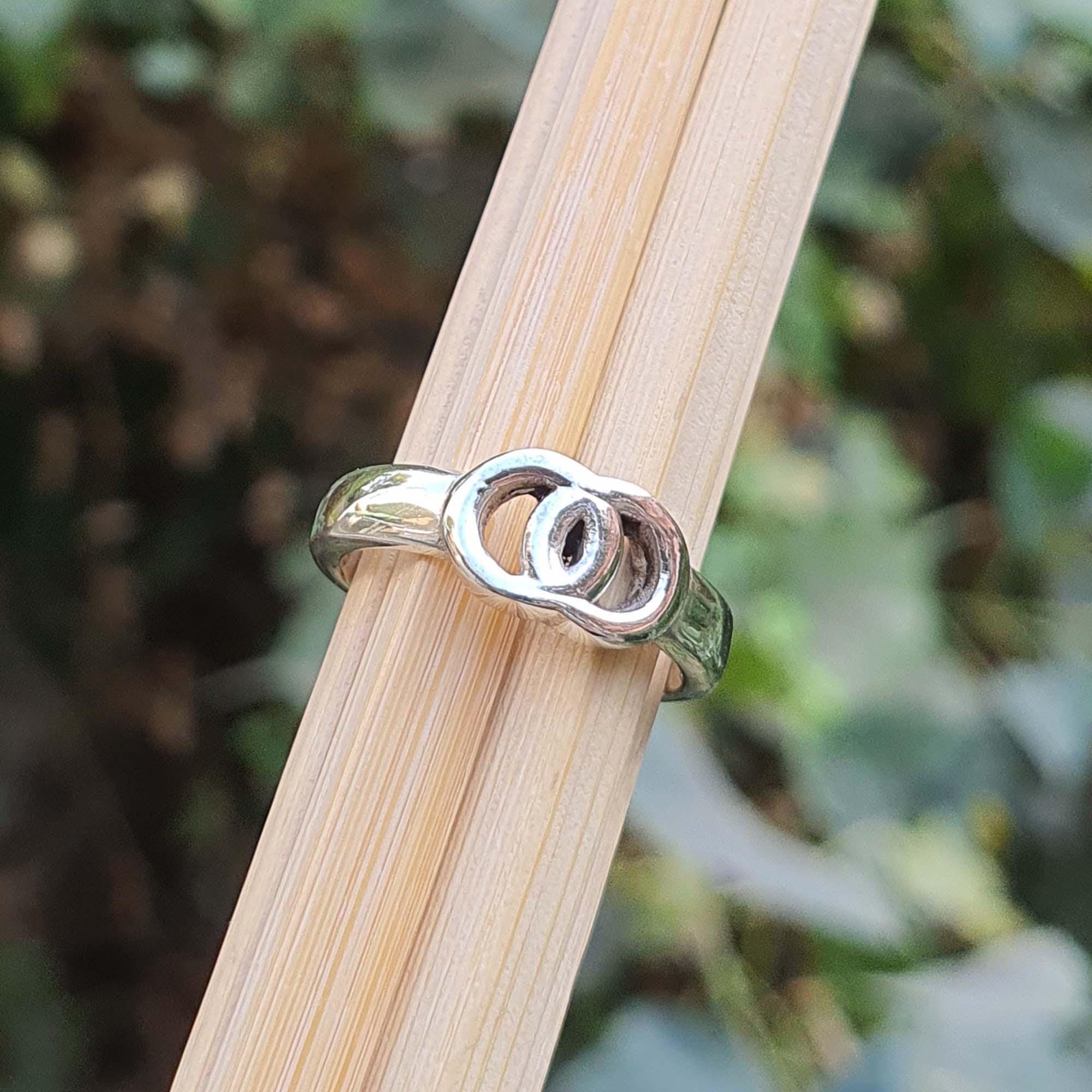 Silver ring with a unique design on a wooden stick against a blurred natural background