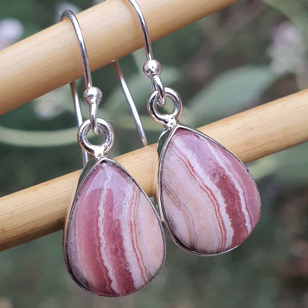 Pink marbled teardrop earrings on a wooden stick with a blurred green background