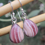 Pink marbled teardrop earrings on a wooden stick with a blurred green background