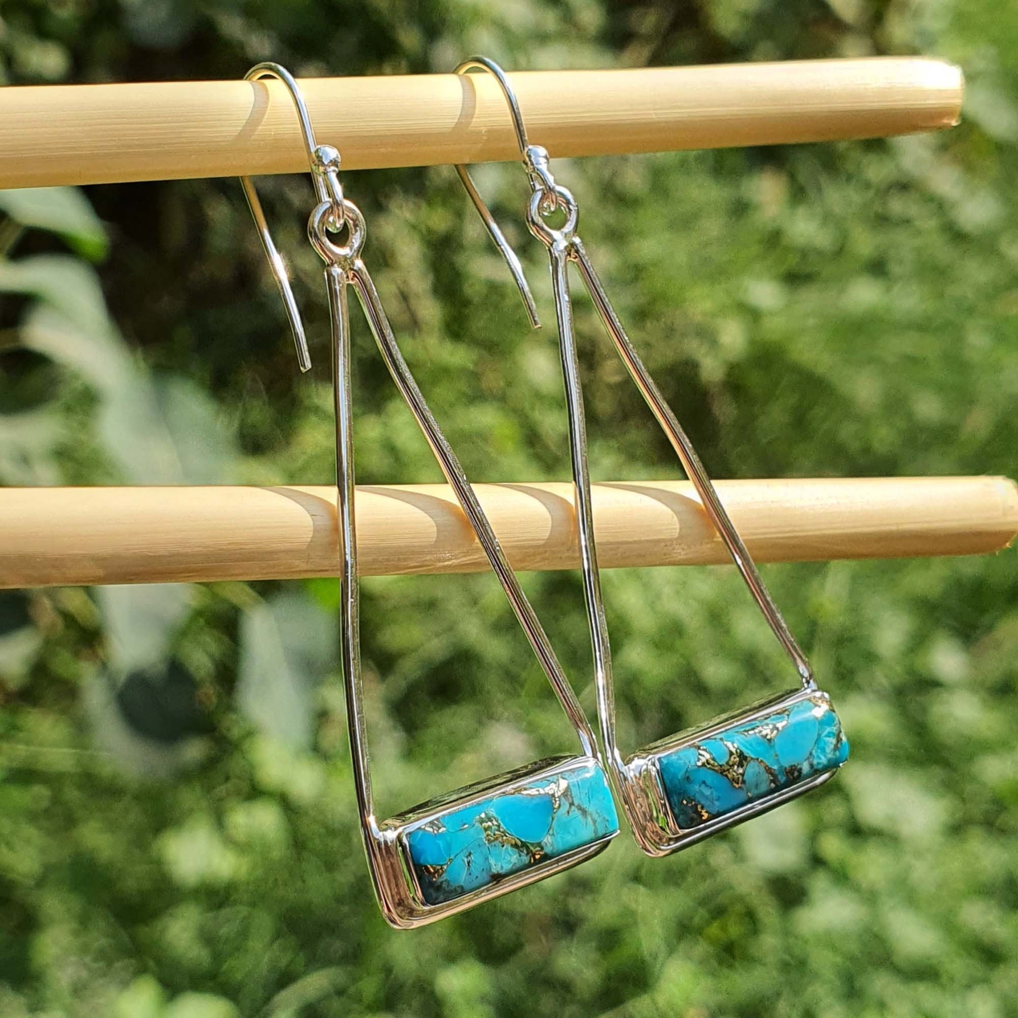 Pair of earrings with turquoise stones on a wooden stick against a green background