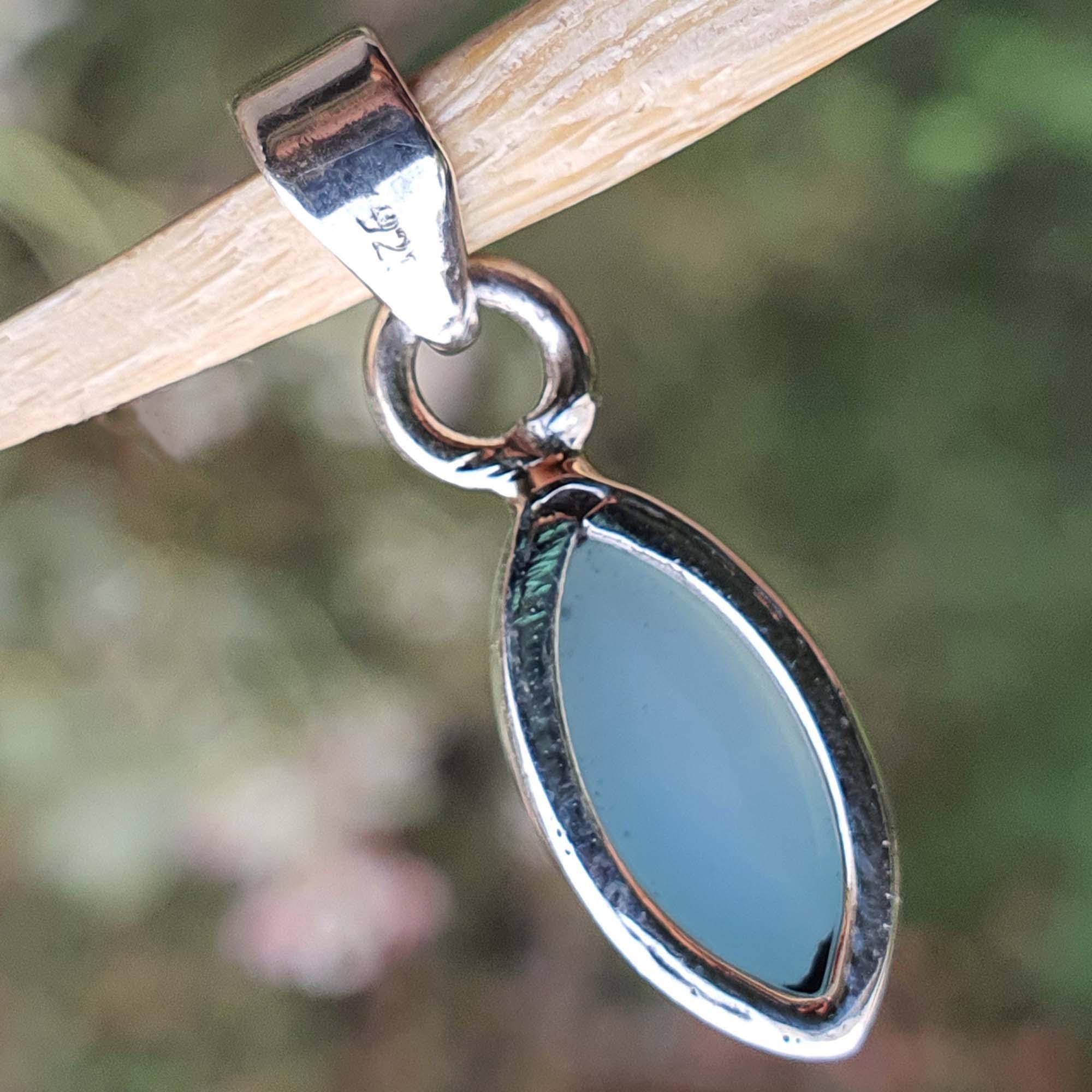 Silver pendant with a blue stone on a blurred natural background