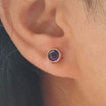 Close-up of an ear with a silver earring featuring a purple gemstone.