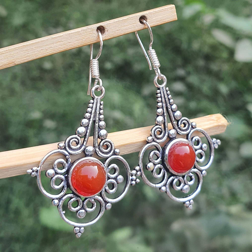 Ornate silver earrings with red stones on a wooden stick against a blurred green background
