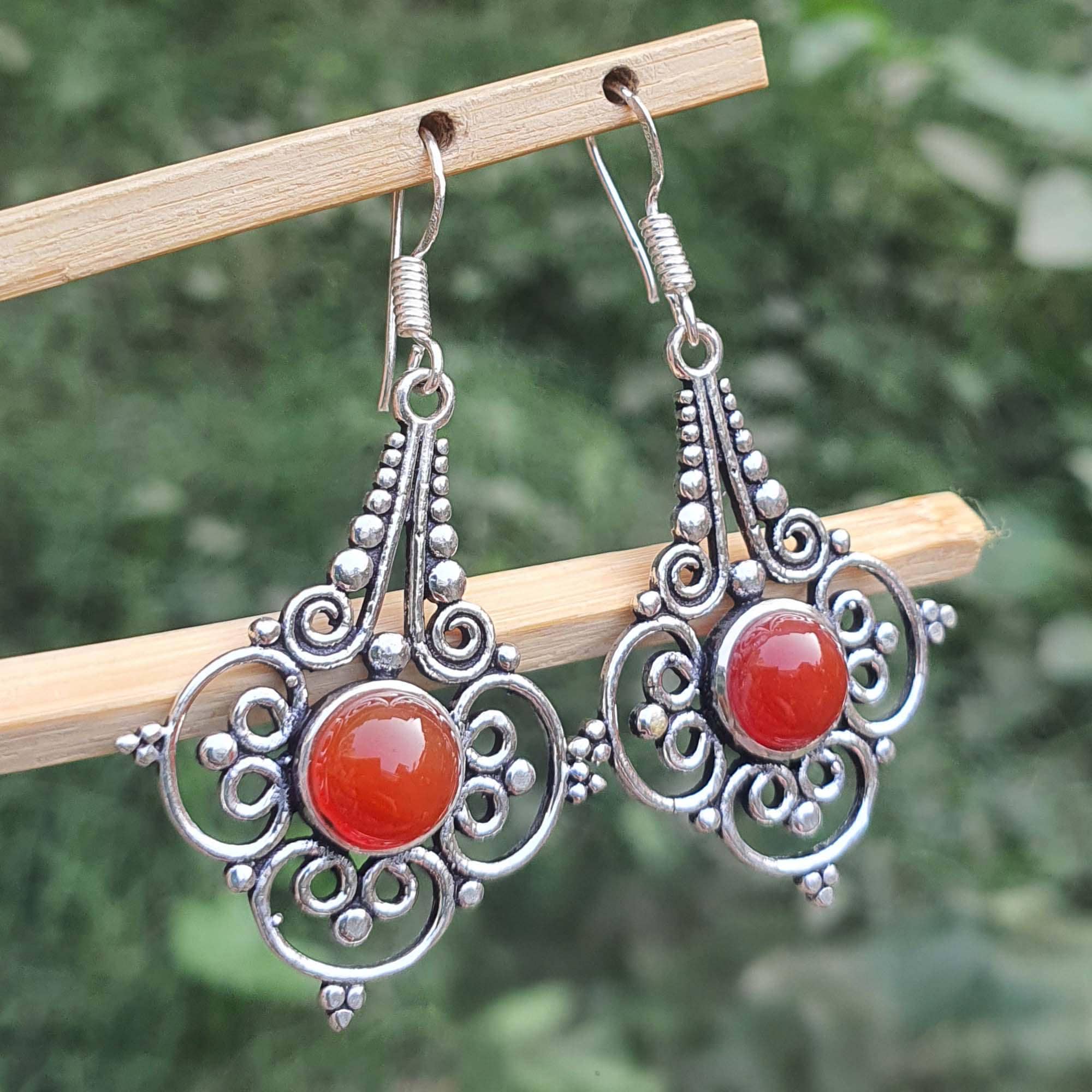 Ornate silver earrings with red stones on a wooden stick against a blurred green background