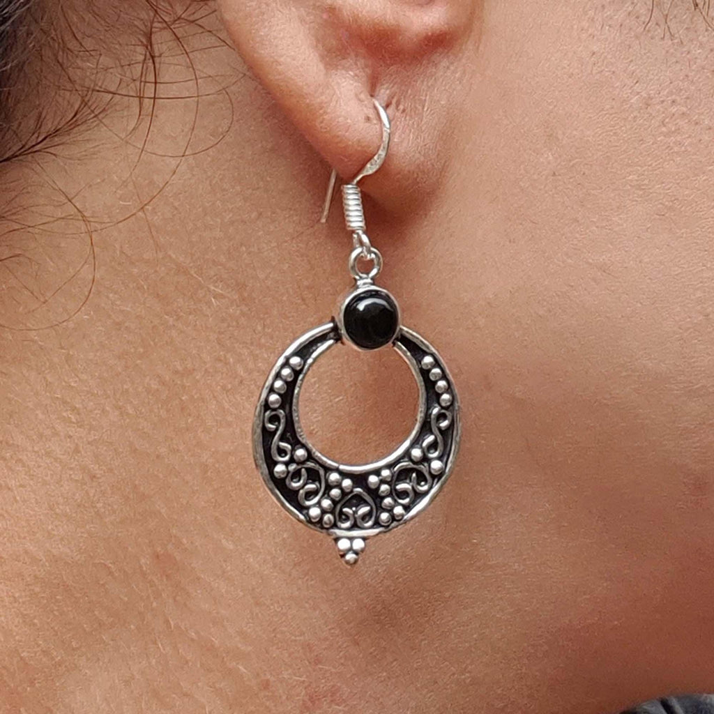 Silver earring with black gemstone worn on an ear