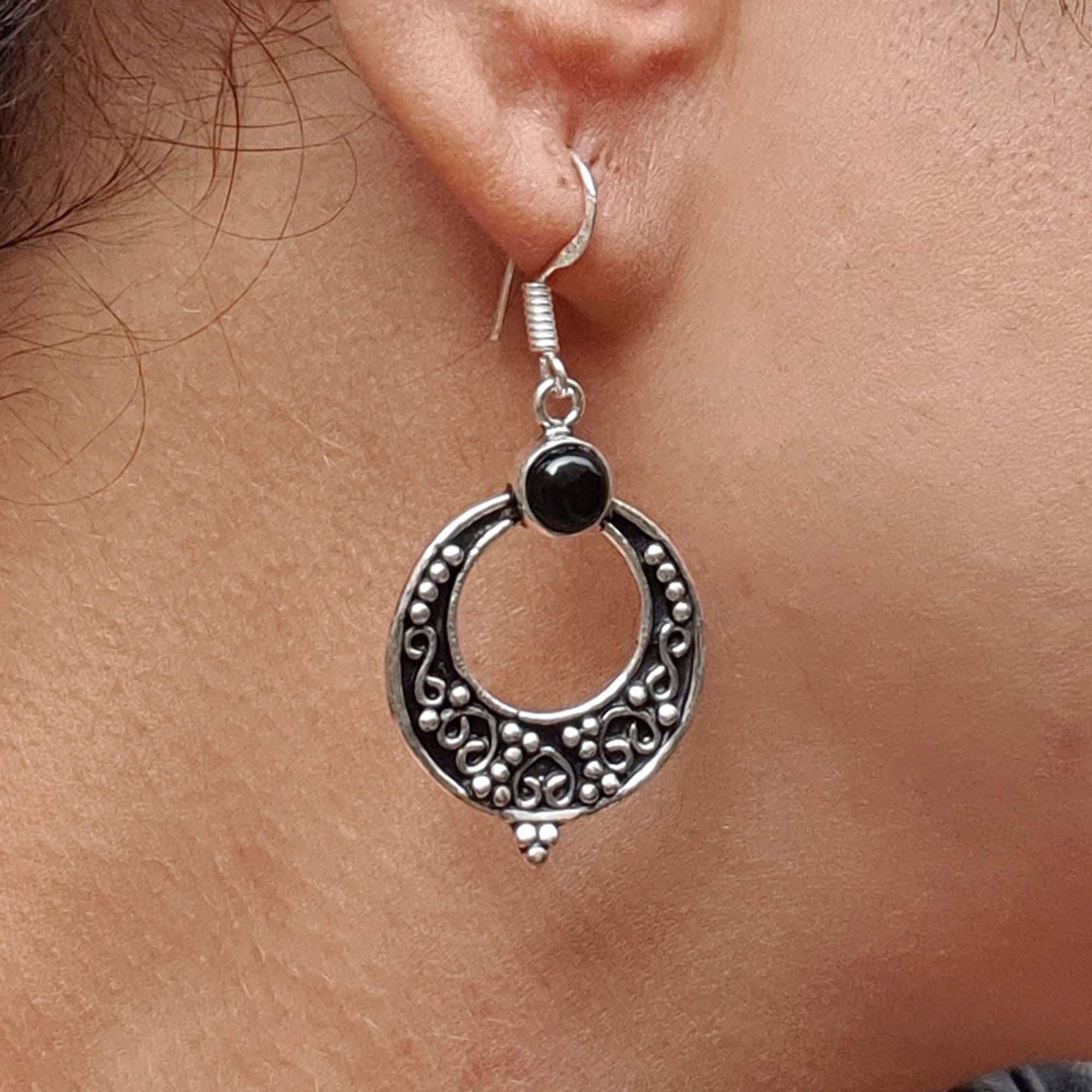 Silver earring with black gemstone worn on an ear
