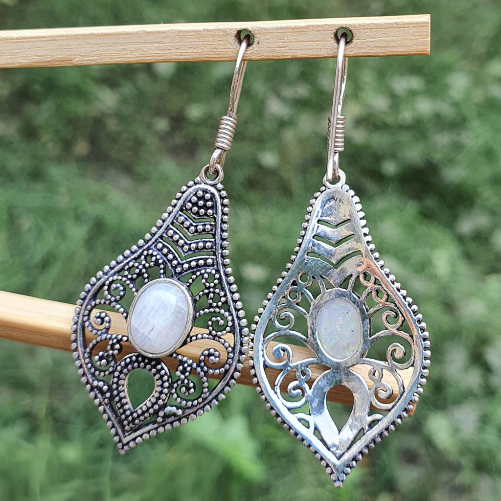Pair of silver filigree earrings with a central gemstone on a wooden stick against a blurred green background.